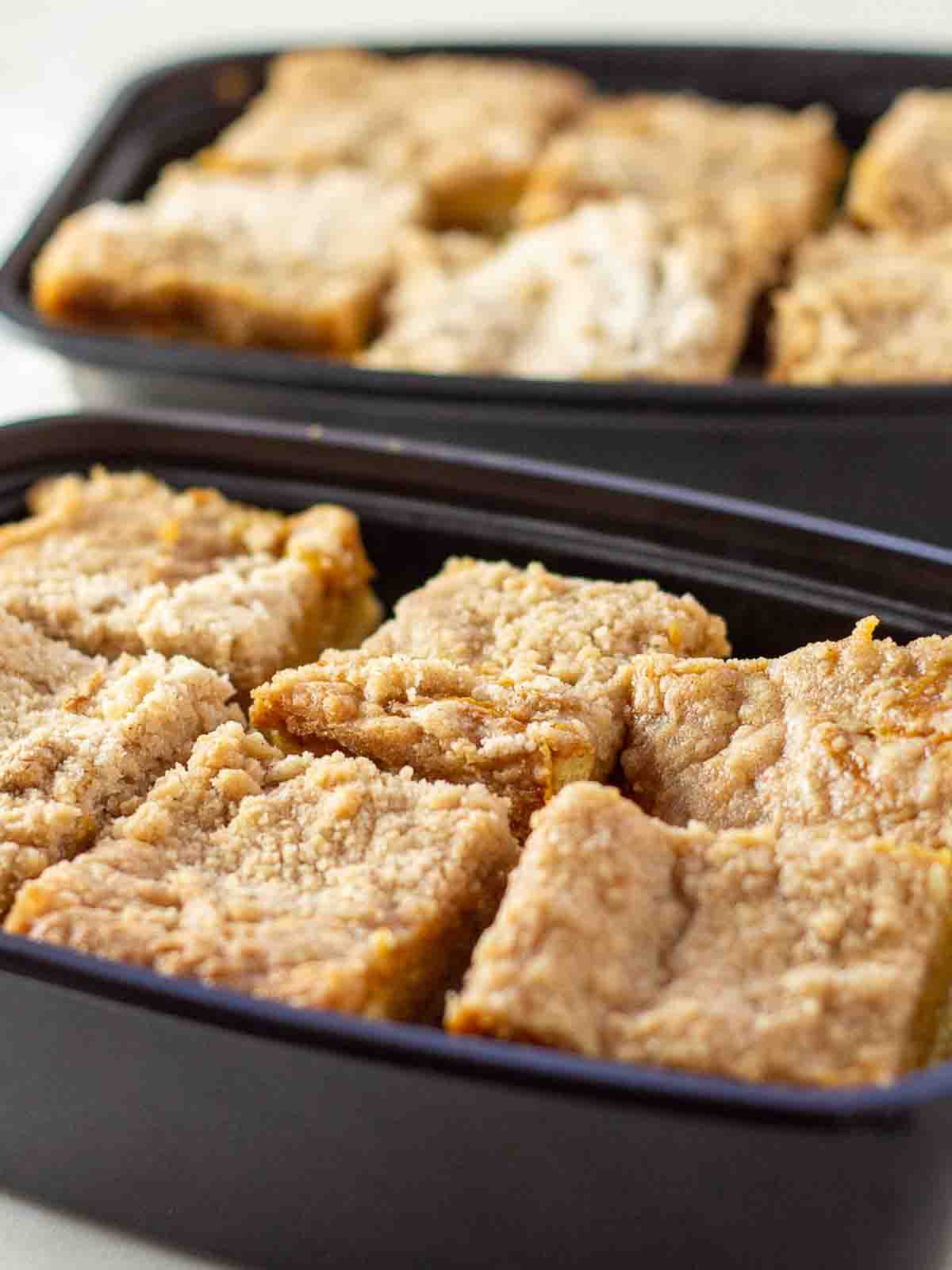 Two plastic containers filled with individually cut pumpkin squares, stacked and ready for the freezer &mdash; perfect for make-ahead fall desserts.
