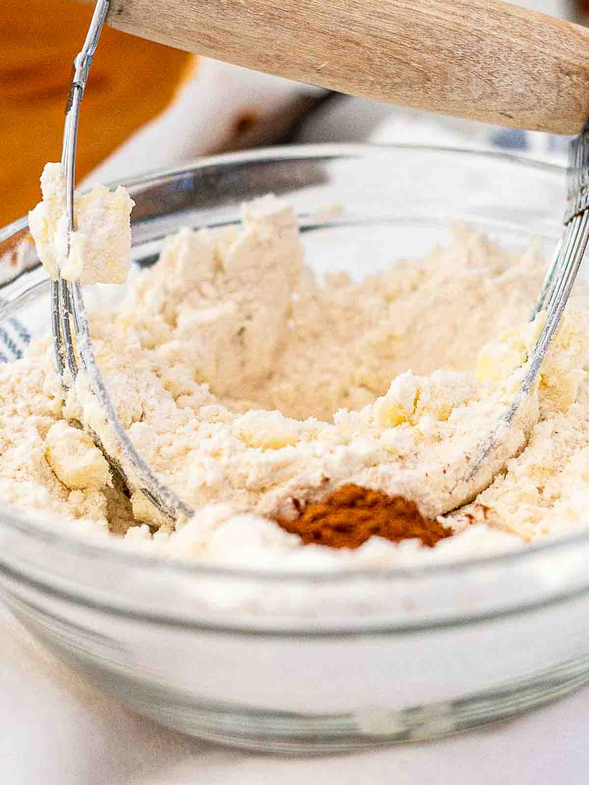 Clear glass bowl with topping ingredients for Williams Sonoma pumpkin bars - cake mix, flour, sugar, cinnamon, and cold butter being cut in with a pastry blender.