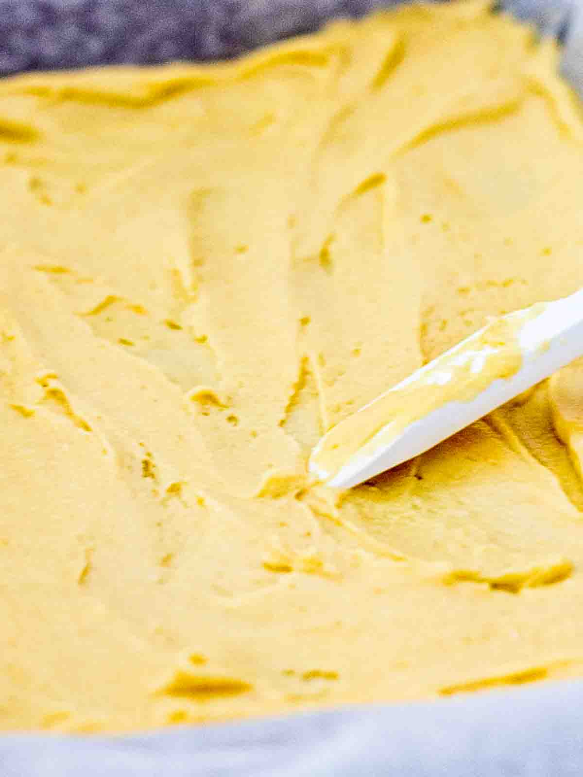 Unbaked bottom layer of Williams Sonoma pumpkin bars in a 9x13 pan - pale, soft dough made from yellow cake mix, butter, and egg, pressed into an even layer.