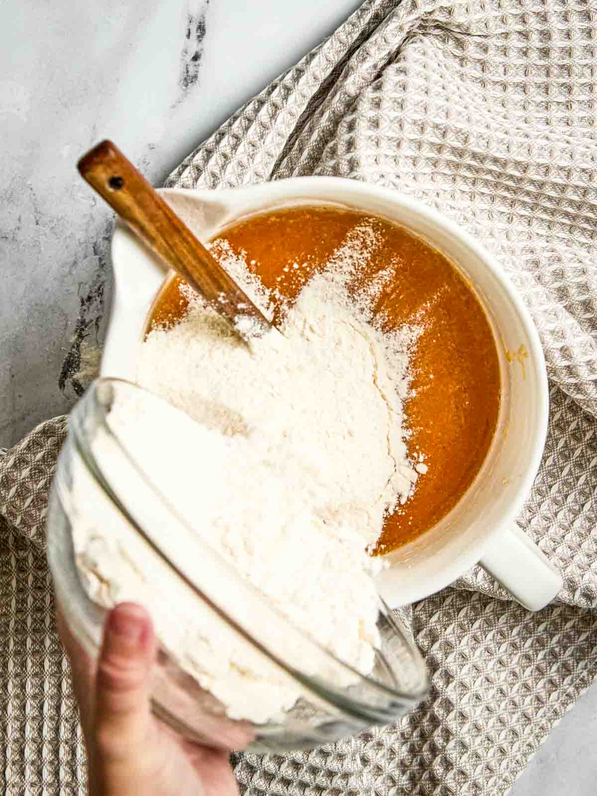 Flour and spices combined together and being poured into a bowl for one-bowl pumpkin bread batter.