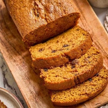 Old-fashioned pumpkin bread loaf sliced on a wooden board, showing moist texture and golden brown crust.