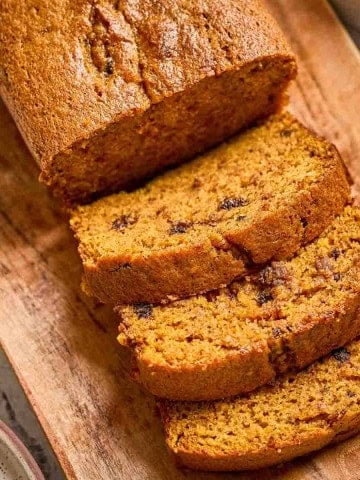 Old-fashioned pumpkin bread loaf sliced on a wooden board, showing moist texture and golden brown crust.