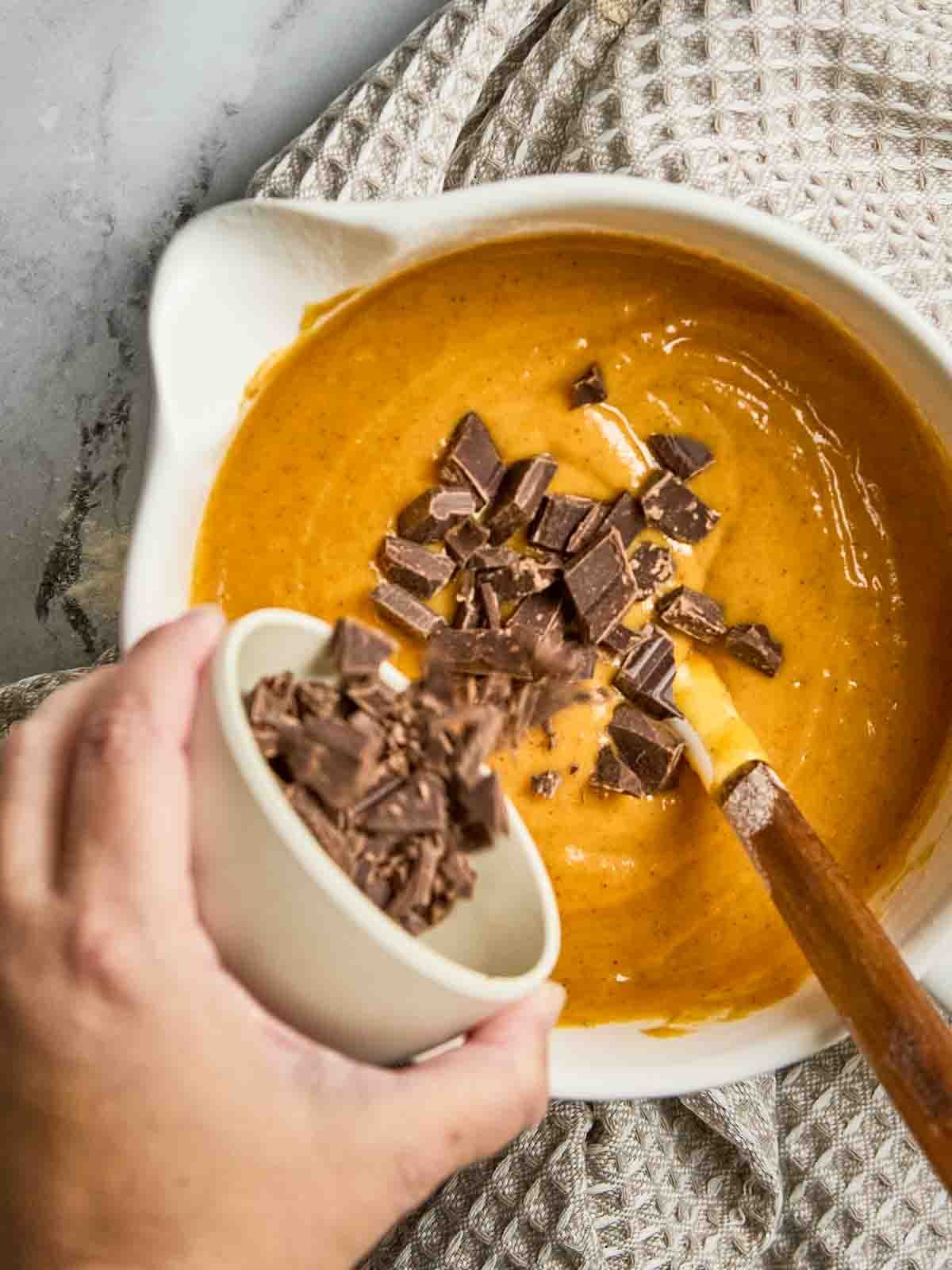 Chocolate chips being poured into pumpkin bread batter in a large mixing bowl.