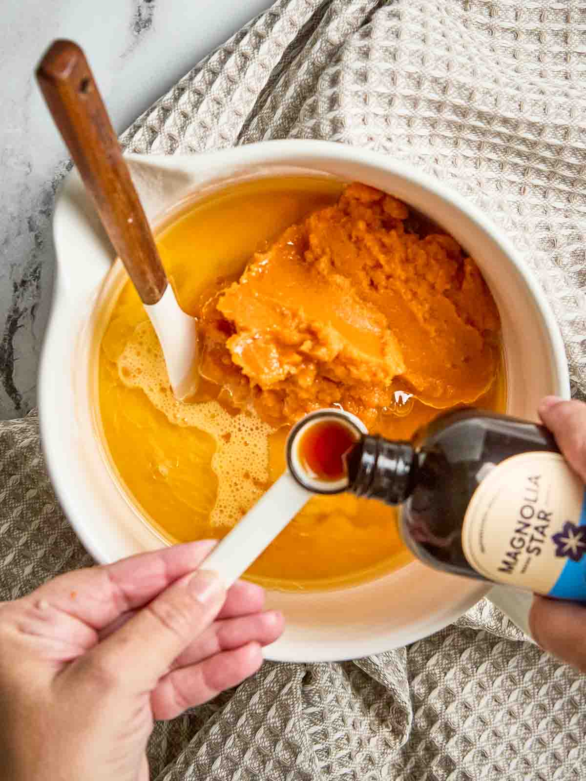 Mixing bowl with sugar, oil, eggs, pumpkin purée, and vanilla stirred by hand.