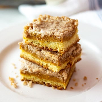 Close-up of three stacked Williams Sonoma pumpkin bars on a white plate, with visible pumpkin butter filling and crumb topping. Fall dessert made with cake mix.
