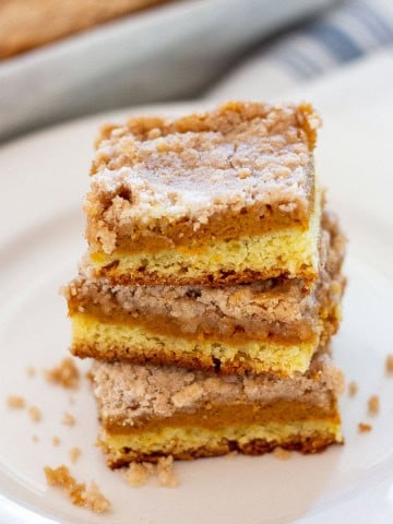 Close-up of three stacked Williams Sonoma pumpkin bars on a white plate, with visible pumpkin butter filling and crumb topping. Fall dessert made with cake mix.