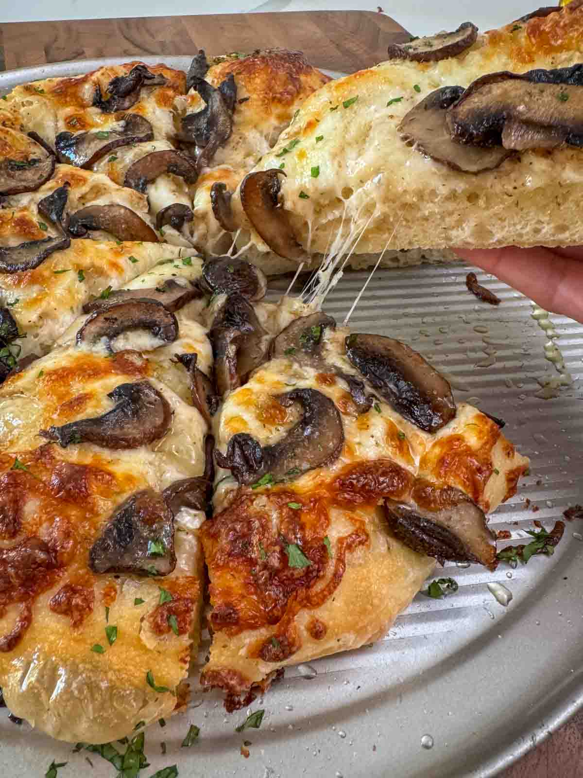 Sliced Homemade white pizza with mozzarella, sautéed mushrooms, and garlic oil with hand pulling up a cheesy slice.