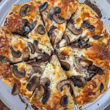 Sliced Homemade white pizza with mozzarella, sautéed mushrooms, and garlic oil.