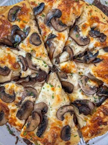 Sliced Homemade white pizza with mozzarella, sautéed mushrooms, and garlic oil.