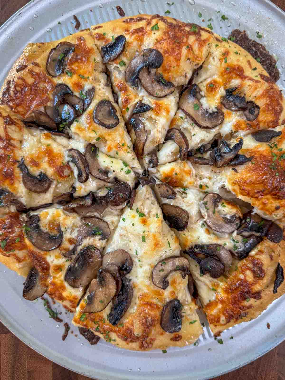 Sliced Homemade white pizza with mozzarella, sautéed mushrooms, and garlic oil.