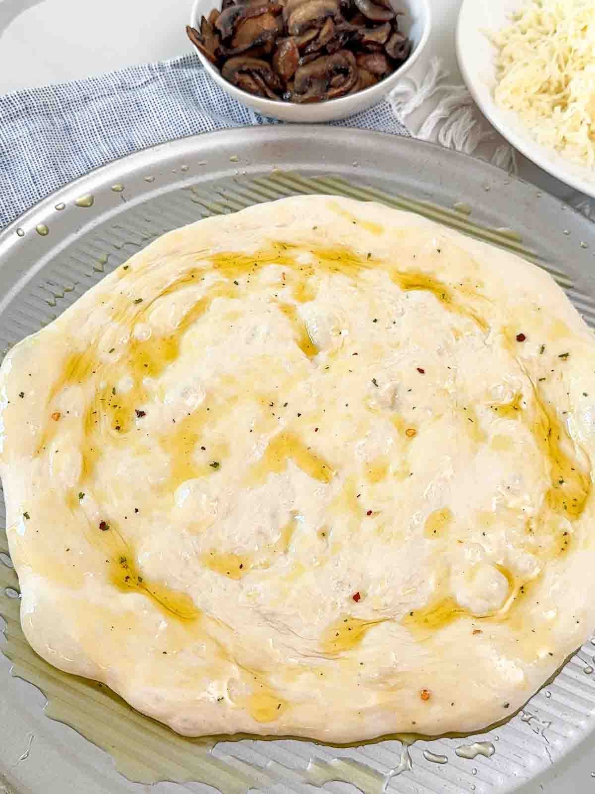 Pizza dough shaped into a round and brushed with garlic olive oil, ready for toppings.