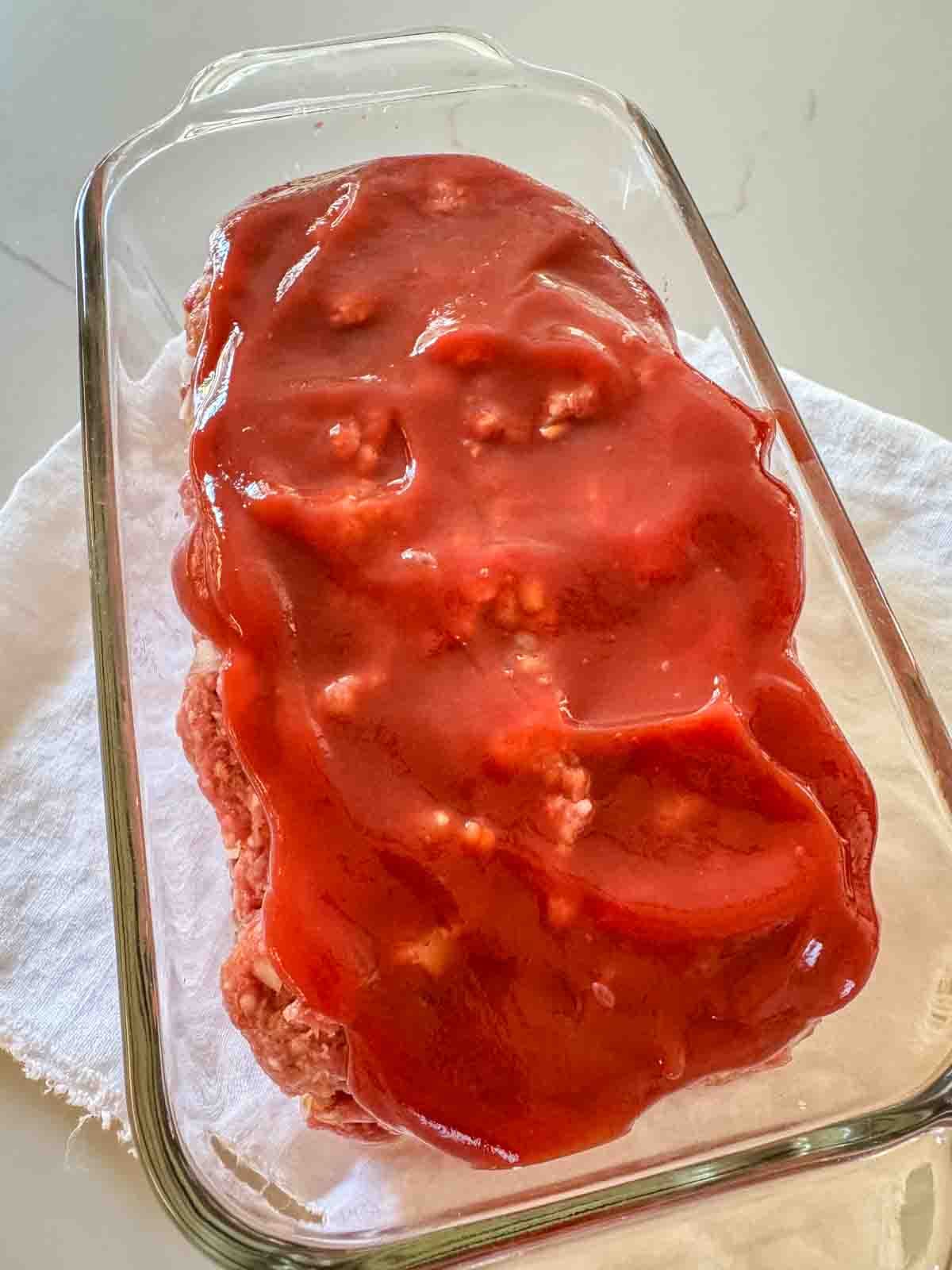 Classic Midwestern meatloaf with ketchup topping in a loaf pan and ready to be baked.