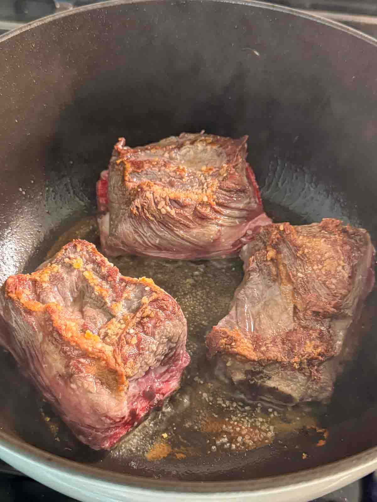 Beef short ribs searing in a Dutch oven until browned.