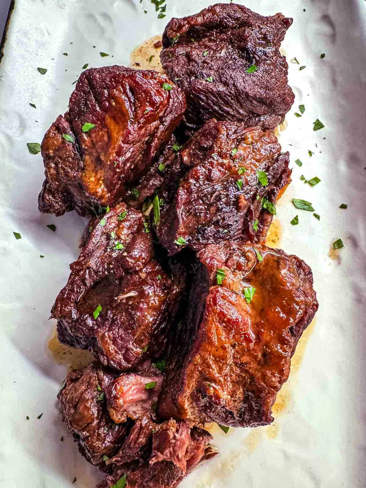 Braised short ribs on a white platter garnished with fresh green parsley.