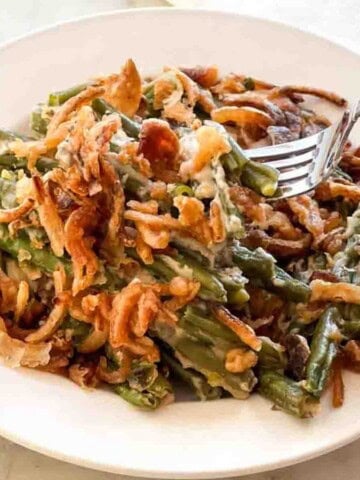A serving of green bean casserole topped with French's crispy fried onions on a white plate.