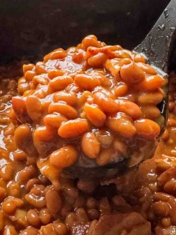 Close-up of homemade baked beans with a rich, glossy sauce, served in a black pot, highlighting the hearty texture and vibrant color.