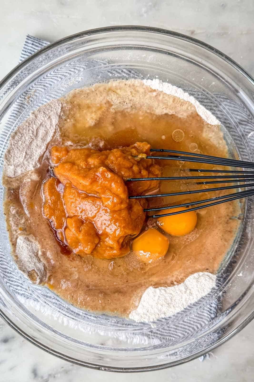 Sugar, oil, eggs, pumpkin puree, water, and vanilla stirred together in a mixing bowl.