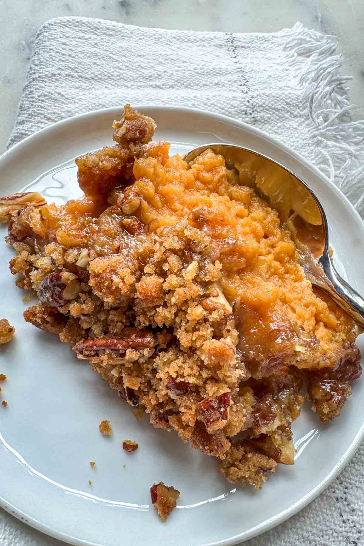 Serving of sweet potato casserole with pecan topping on a white plate.