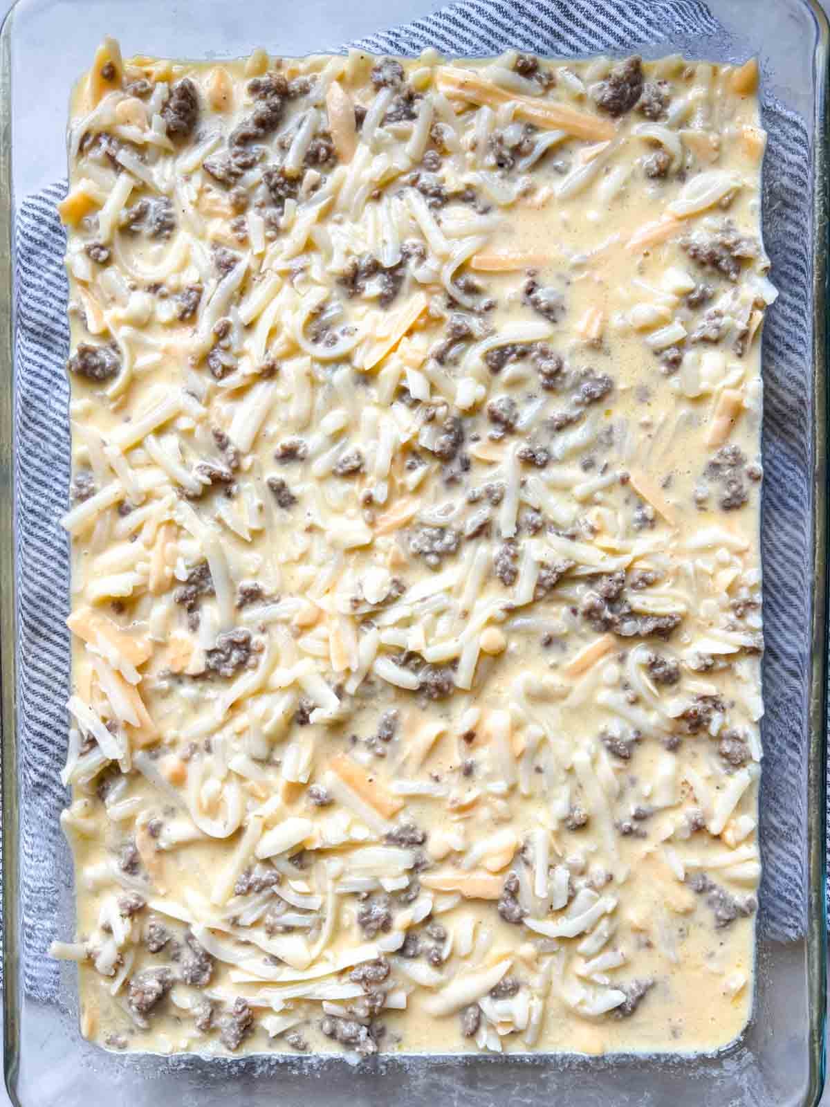 Unbaked sausage hash brown breakfast casserole topped with shredded cheddar.